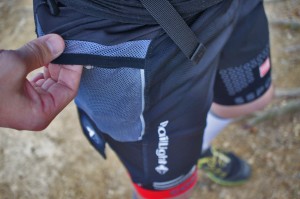 上写真のミックスナッツの袋を入れた上で、（上写真の）ランニンググローブを収納したイメージ。結構入っていますが、ストレッチ性の背面とポケットメッシュにより、走っていても違和感は感じない。指をかけているのはフラップ部分。ポケット口とオーバーラップしている。